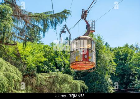 Alte verlassene Seilbahnkabine, die an einer stillgelegten Seilbahn in der Stadt Chiatura, Georgien, hängt. Sowjetische Infrastruktur, industrielles Erbe, urbaner Verfall Stockfoto