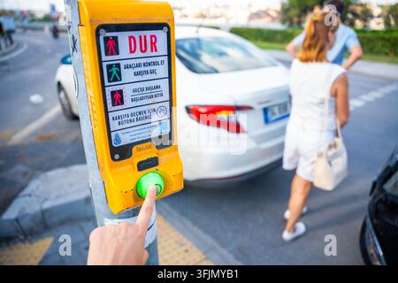 Istanbul, Türkei – 28. August 2026: Fußgängerampeltaste wird gedrückt, während Autos und Fußgänger in einer städtischen Straßenszene sichtbar sind Stockfoto