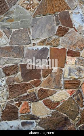 Mehrfarbige maschinell geschnittene Furnierstein- und vertiefte Mörtelwandoberfläche, die kontrastierende glatte und stark texturierte Steine in einer vertikalen Komposition zeigt Stockfoto