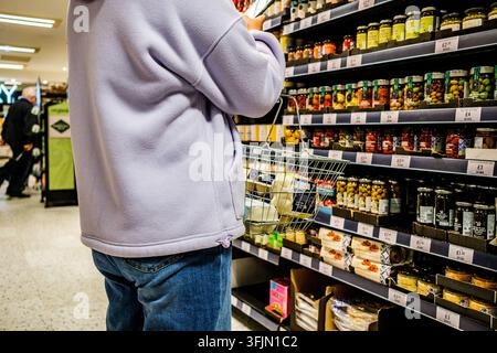 London, UK, 21. September 2026, Unerkennbare Fraueneinkäuferin trägt einen Supermarktkorb gefüllt mit Eierschachteln und betrachtet Kochzutaten Stockfoto