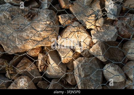Gabionenmauer aus Natursteinen in Drahtgeflecht unter einem Sonnenstrahl Stockfoto