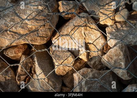 Gabionenmauer aus Natursteinen in Drahtgeflecht unter einem Sonnenstrahl Stockfoto