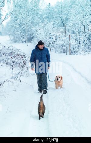 Ein Mann mit Hund an der Leine geht im Winterwald entlang der Straße Stockfoto