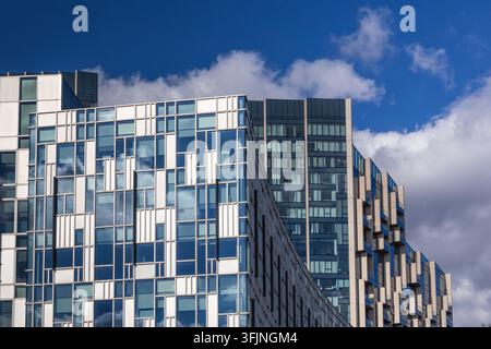 Geometrische Glasfassade eines Firmenhochhauses vor blauem Himmel und weißen Wolken Stockfoto