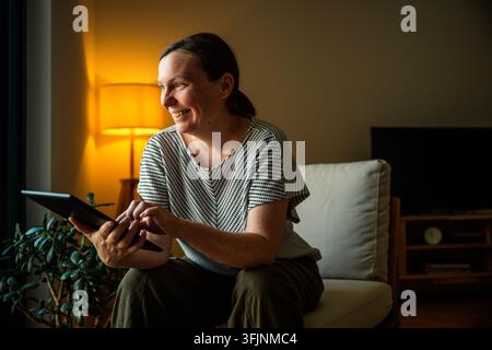 Zufriedene, glückliche reife Frau lächelt und nutzt ein Digitales Tablet zu Hause. Selektives Zuhause. Stockfoto