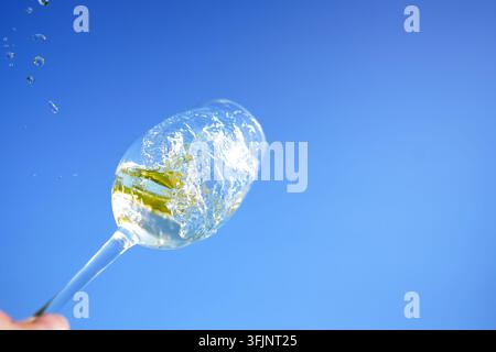 Weißwein im Glas wirbelt vor blauem Himmel. Sommelier wirbelt mit Weinglas vor Sonnenuntergangshimmel. Weißwein wirbelt im Glas während der Weinverkostung, celebra Stockfoto