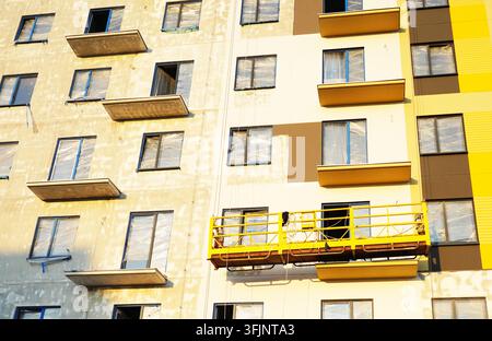 Hängende Baukrone an der bemalten Fassade eines Gebäudes. Mobile Gerüstplattform für Bauarbeiten in der Höhe, Fassadentreinigung, Verputzen Stockfoto