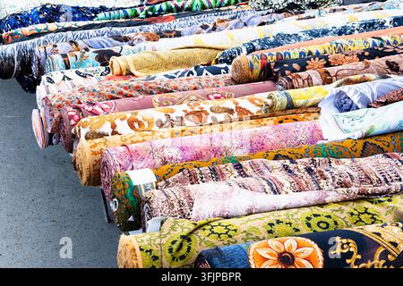 Bunte Stoffrollen, die auf einem Freiluftbasar in Buxara, Usbekistan, ausgestellt sind. Dutzende von gemusterten Textilien mit Blumen- und Ikat-Mustern schaffen eine lebhafte Stockfoto