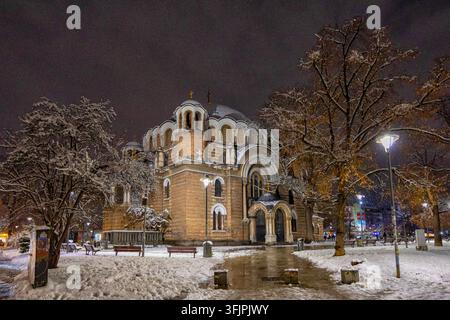 Blick auf die Saint-Nedelya-Kirche bei Nacht, beleuchtet während eines Wintersturms mit schneebedeckten Bäumen und Bänken im umliegenden Park in Sofia, Sofia Stockfoto