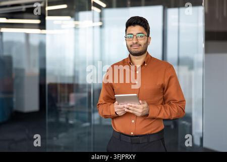 Professioneller Geschäftsmann hält ein Tablet in einem modernen Büro, junger indischer Unternehmer nutzt ein digitales Gerät für Finanzanalysen und Unternehmenskommunikation am Schreibtisch für Geschäftswachstum. Stockfoto