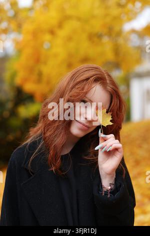 Fröhliches Frauenporträt mit Ahornblättern, das einfache Freuden, Selbstfürsorge und positive Emotionen im Freien darstellt. Stockfoto