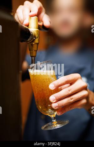 Nahaufnahme einer Actionaufnahme eines Barkeepers, der einen Metall-Zapfhahn bedient, um ein klares Glas mit kaltem goldenem Bier zu füllen. Stockfoto
