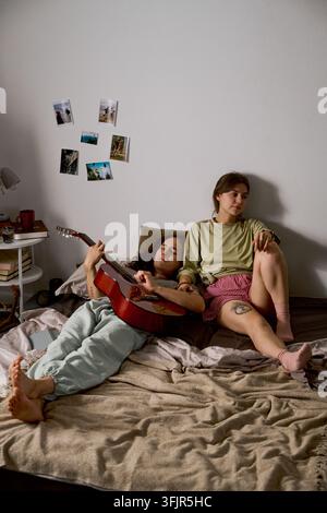 Romantisches Paar entspannt sich auf dem Bett, während der Mann Akustikgitarre spielt Stockfoto