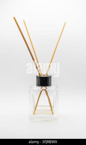 Minimaler Heimduft-Rohrstabdiffusor mit Holzstäbchen in einer transparenten quadratischen Flasche auf einem sauberen weißen Hintergrund. Stockfoto