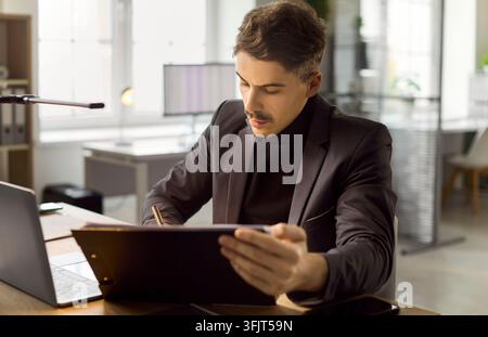 Geschäftsprofi überprüft Klemmbrett am Laptop in einem hellen modernen Büro Stockfoto