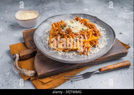 Rustikale Nudelbolognese mit reichhaltigem Fleisch-Ragu und Parmesan, serviert auf einer grauen Teller über strukturiertem Betonhintergrund mit Gabel Stockfoto