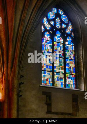 Kircheninneres zeigt das beeindruckende gewölbte gotische Fenster mit zeitgenössischem abstraktem Design aus Buntglas, das den historischen Bogen hell erleuchtet Stockfoto