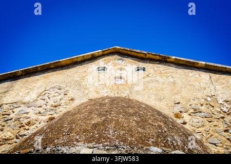 Niedrigwinkelaufnahme eines alten Kirchen Firstes und einer strukturierten Steinmauer unter einem klaren blauen Himmel in Kreta, Griechenland Stockfoto