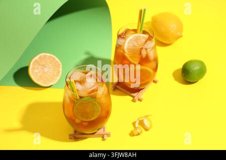 Gläser mit leckerem kaltem Eistee mit Zitrone und Limette auf gelbem Hintergrund Stockfoto