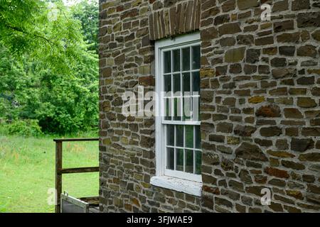 Ein historisches Steinmauergebäude mit einem weißen Fensterrahmen, das sich vor einem üppigen grünen Außenhof abhebt. Stockfoto