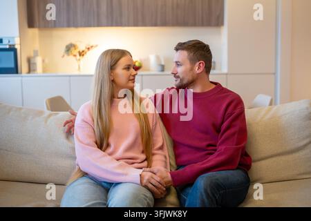 Verliebtes Ehepaar, Mann und Frau, die sich umarmend zusammen auf der Couch im Wohnzimmer zu Hause sitzen. Stockfoto