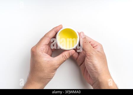 Oberansicht von Händen, die eine kleine Keramik Tasse mit heißem Oolong-Tee halten, isoliert auf weißem Hintergrund mit Kopierraum Stockfoto