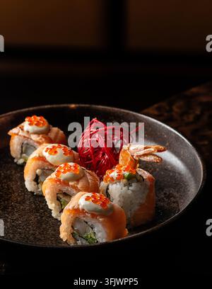 Gourmet-Lachs-Sushi-Rollen, belegt mit cremiger Sauce, rotem Kaviar und Ebi-Tempura-Garnelen in einer dunklen Keramikschale. Stockfoto