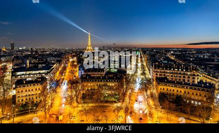 Paris, Frankreich – 04. Januar 2026: Nachtansicht der Pariser Stadtlandschaft mit dem beleuchteten Eiffelturm und einem Lichtstrahl über den Himmel. Stockfoto