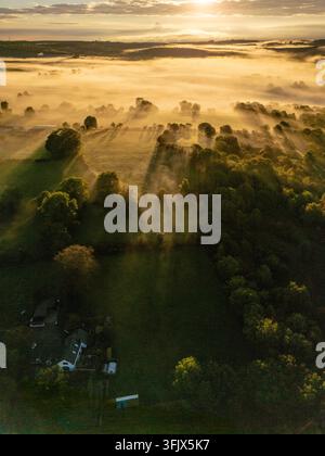 UK-Wetter: Dienstag, 22. September 2026, früher Morgennebel und tiefe Wolken bilden sich über der hügeligen Landschaft des ländlichen Flintshire, während ein atemberaubender goldener Sonnenaufgang die grünen Felder, die mosaikartigen Hügel und Täler in der Nähe der Clwydian Range in warmes Morgendlicht taucht, Nordwales, UK Stockfoto