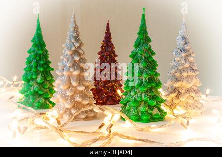 Dekorative kerzenförmige Weihnachtsbäume stehen auf einer hellen Oberfläche, umgeben von einer leuchtenden Lichterkette. Stockfoto