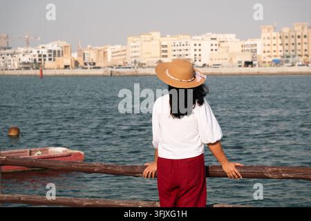 Frau entspannt sich am Ufer des Dubai Creek und bewundert die historische Skyline von Deira in den VAE Stockfoto