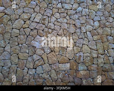 Rustikale trockene Steinmauertextur aus unregelmäßigen braunen Feldsteinen für Hintergrund und Design Stockfoto