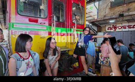 SAMUT SONGKHRAM, THAILAND - 14. MARZ 2026: Touristen posieren für Fotos auf den Stufen eines stillstehenden SRT-Zugs am berühmten Maeklong-Bahnhofsmarkt in Samut Songkhram Stockfoto