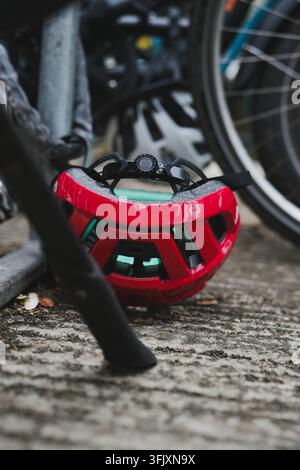 Roter Fahrradhelm, der auf dem Boden zwischen Fahrradrädern ruht Stockfoto