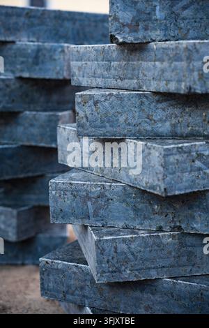 Nahaufnahme Seitenansicht von gestapelten schweren polierten grauen Granitsteinplatten, die für Außenpflasterungen und Baudekoration auf einer Baustelle vorbereitet sind. Stockfoto