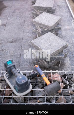 Professionelle Fliesenverlegungswerkzeuge einschließlich Gummihammer und Saugvibrator, die auf einer Baustelle mit gestapelten Granitpflastersteinen platziert sind Stockfoto