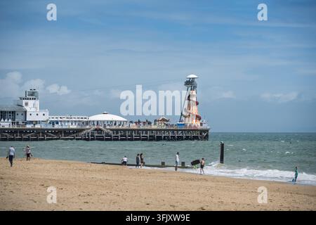 Ein weitläufiger Blick auf Touristen am Sandstrand, die in Richtung des historischen Bournemouth Piers und seiner Helter Skelter Attraktion in Dorset, England, UK blicken Stockfoto