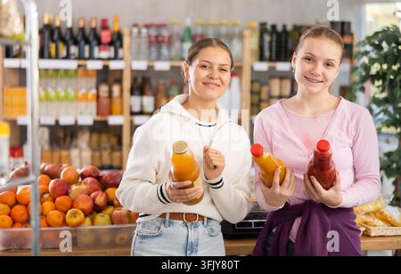 Zwei junge Käuferinnen wählen Pfirsich- und Tomatensaft im Supermarkt Stockfoto