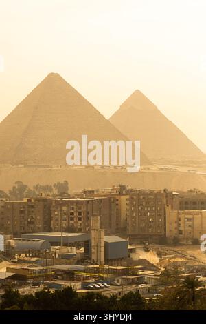 Eine Ansicht von Kairo-Stadtgebäuden und den Gizeh-Pyramiden, die in der Ferne von orangefarbenem Wüstensand bedeckt sind. Stockfoto