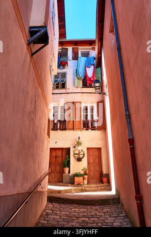 Sonnenbeleuchtete enge Gasse mit hängender Wäsche, Holzläden und Kopfsteinpflasterstufen in der Altstadt von Isola Stockfoto