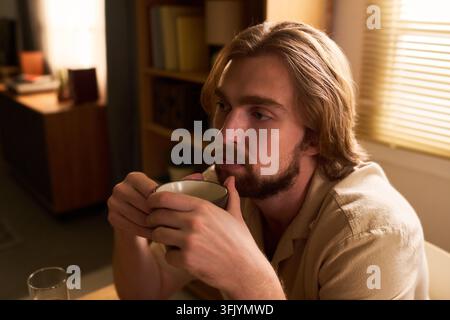 Nachdenklicher Mann trinkt Kaffee während der Morgenroutine zu Hause Stockfoto