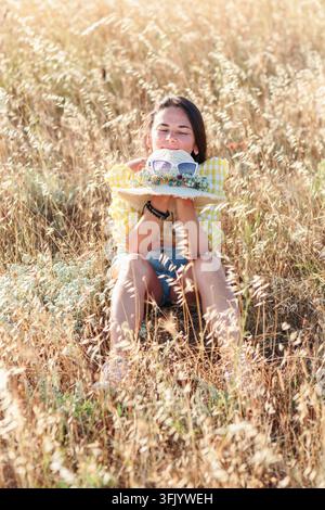 Glückliche Frau entspannt sich auf einer goldenen Wiese mit Strohhut Stockfoto