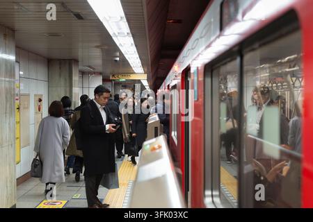 Pendler steigen in einen roten Zug der Tokyo Metro Marunouchi-Linie auf dem U-Bahn-Gleis des Bahnhofs Tokio in Tokio, Japan, für den täglichen Pendelverkehr. Stockfoto