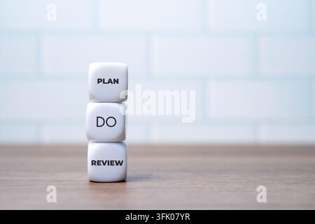 Gestapelte weiße Würfel mit den Worten PLAN, DO und REVIEW auf einem Holzschreibtisch. Geschäftsmanagement-Zyklen, strategische Umsetzung, Workflow-Konzept. Stockfoto