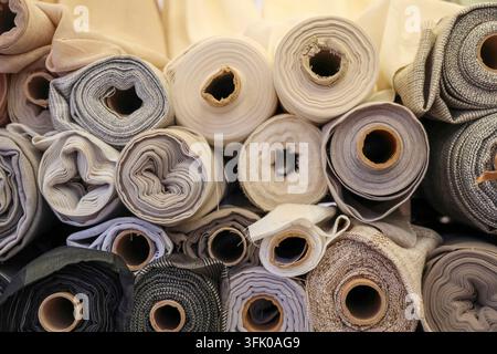 Verschiedene Stoffrollen gestapelt, wodurch ein strukturierter Hintergrund mit neutralen Farben entsteht Stockfoto