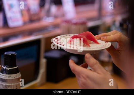 Eine Person hält einen Teller mit frischem Thunfisch-Sushi bei Sushiro in Tokio, Japan, um eine Mahlzeit auf dem Förderband zu genießen. Stockfoto