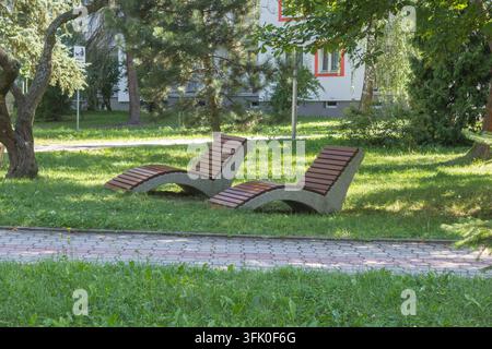 Zwei Holzsonnenliegen auf einem grasbewachsenen Rasen in einer grünen Parkumgebung. Stockfoto