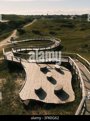 Erhöhter Holzsteg mit Ruheplattformen windet sich durch grüne Dünen auf Norderney, ideal für Naturtourismus und Ökologie-Konzepte. Stockfoto