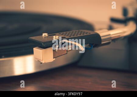 Ein Plattenteller-ZTonarm und eine Nadel liegen neben einem Vinyl-Plattenspieler mit warmem Umgebungslicht auf einer Holzoberfläche Stockfoto
