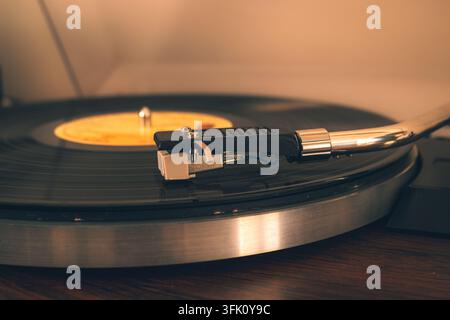 Ein Plattenteller-Z Tonarm und eine Nadel sitzen auf einer sich drehenden Vinylplatte, beleuchtet von warmem Umgebungslicht auf einer Holzoberfläche Stockfoto